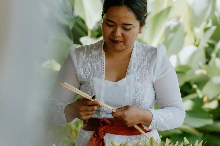 Balinese woman crafting canang offerings from palm leaves
