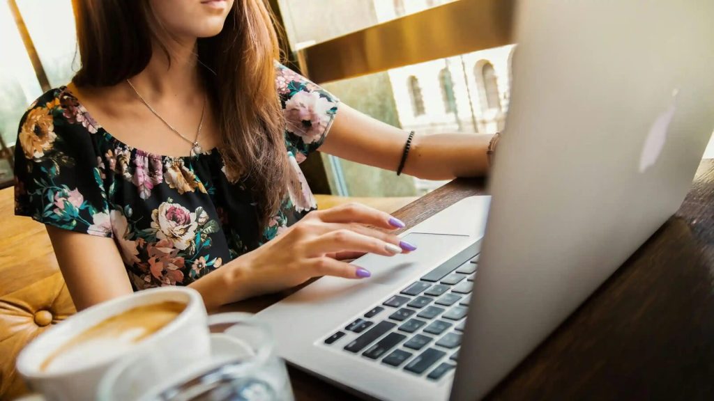 Remote worker typing on a laptop beside a cup of coffee